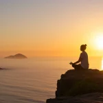 Mindfulness para ansiedade: 5 estratégias essenciais no Brasil em 2025 Pessoa meditando ao nascer do sol, representando mindfulness e tranquilidade em paisagem brasileira.