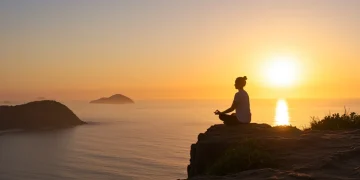 Pessoa meditando ao nascer do sol, representando mindfulness e tranquilidade em paisagem brasileira.