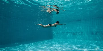 Pessoa nadando em piscina, demonstrando a fluidez e o benefício da natação para a saúde.